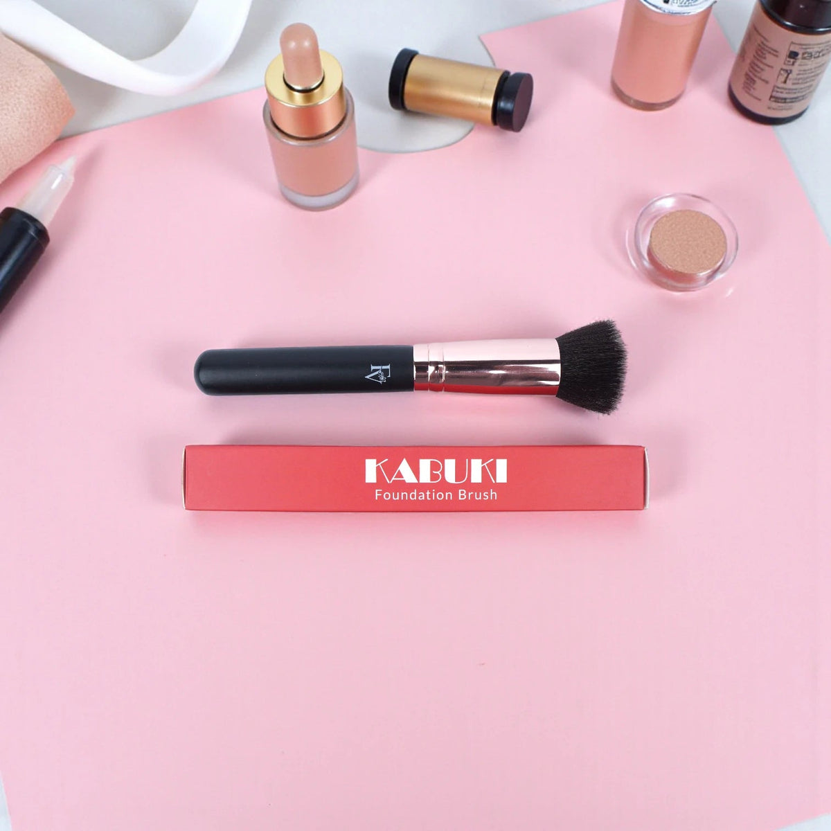 FV Skin Studio Kabuki brush with black handle and soft bristles, displayed with its red packaging on a pink surface.